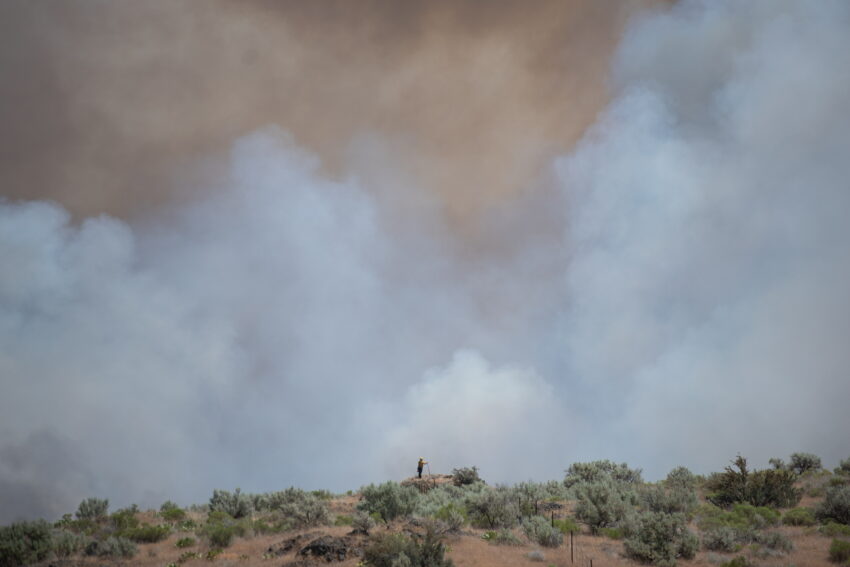Photo of the Hat Rock Fire showing smoke and a firefighter in the distance.