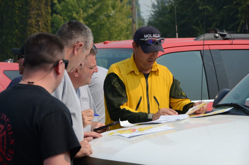 Firefighters looking at a map and other documents on the hood for an SUV.