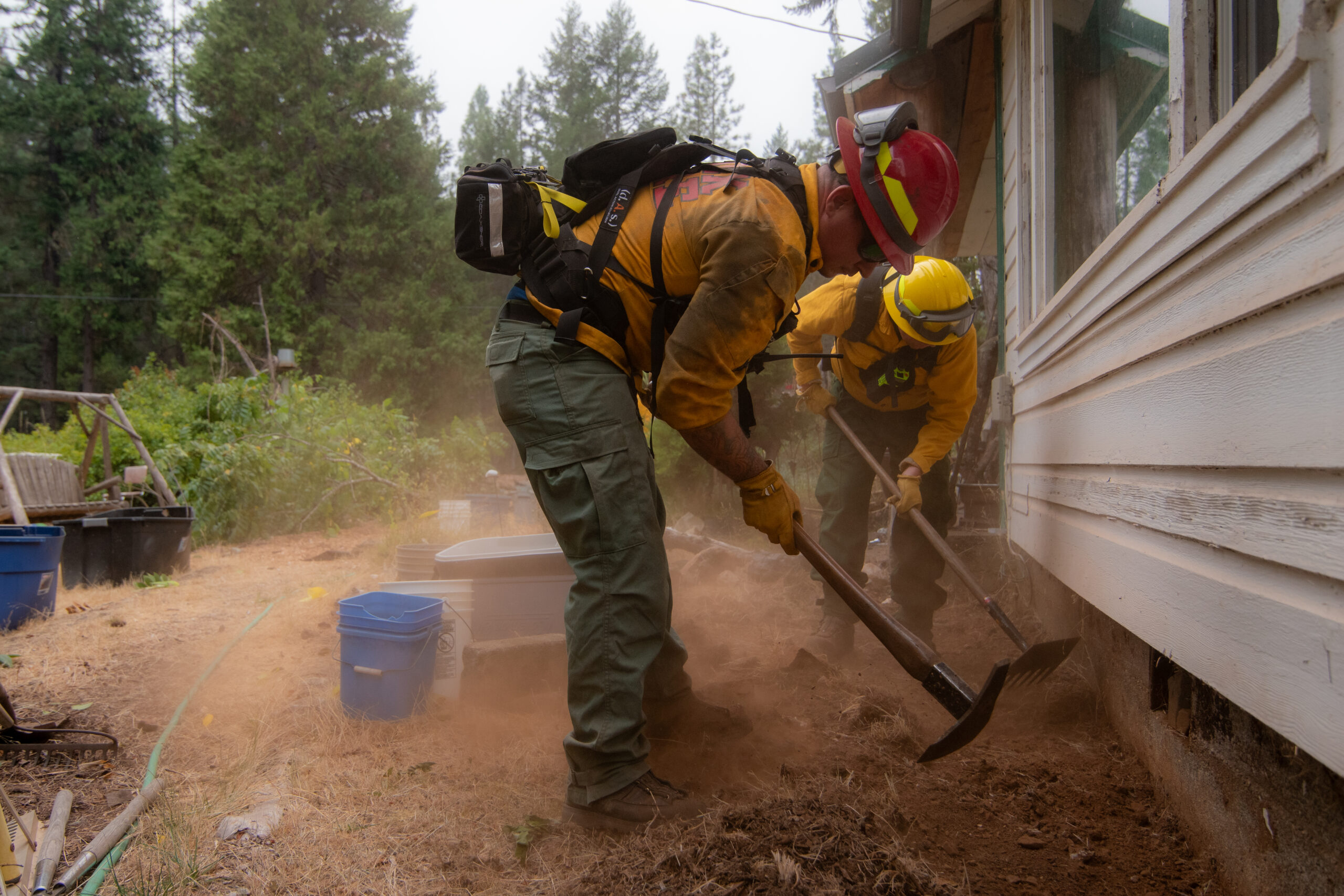 firefighters moving grass and plants away from the base of a home
