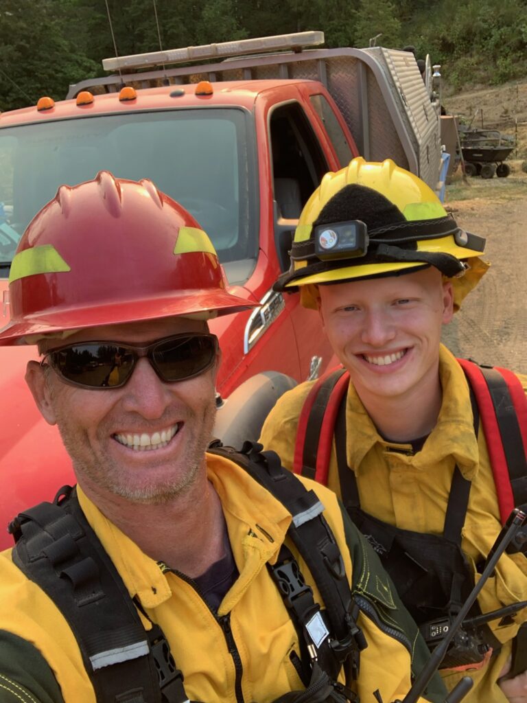 Two people standing next to each other smiling for a photo. They are both dressed in wildland firefighting gear