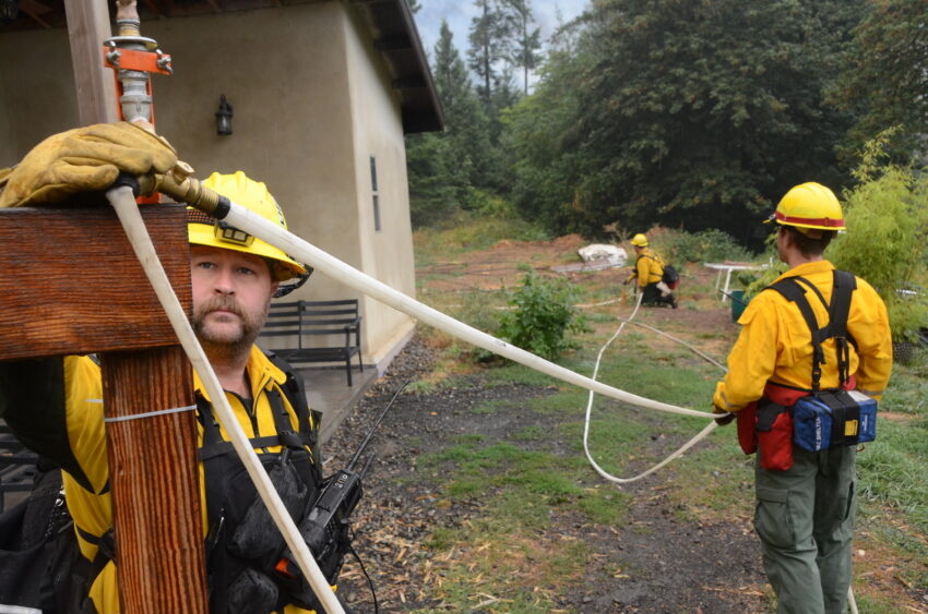 Firefighters setting up a sprinkler system on a home near a wildfire on the Tyee Ridge Complex.