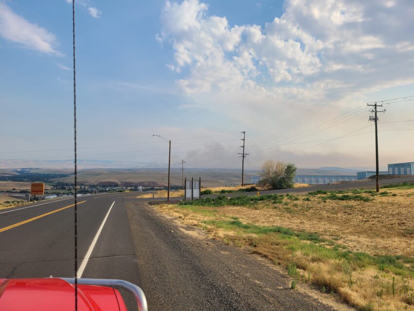 Photo looking out from a vehicle at a wildfire in the background.