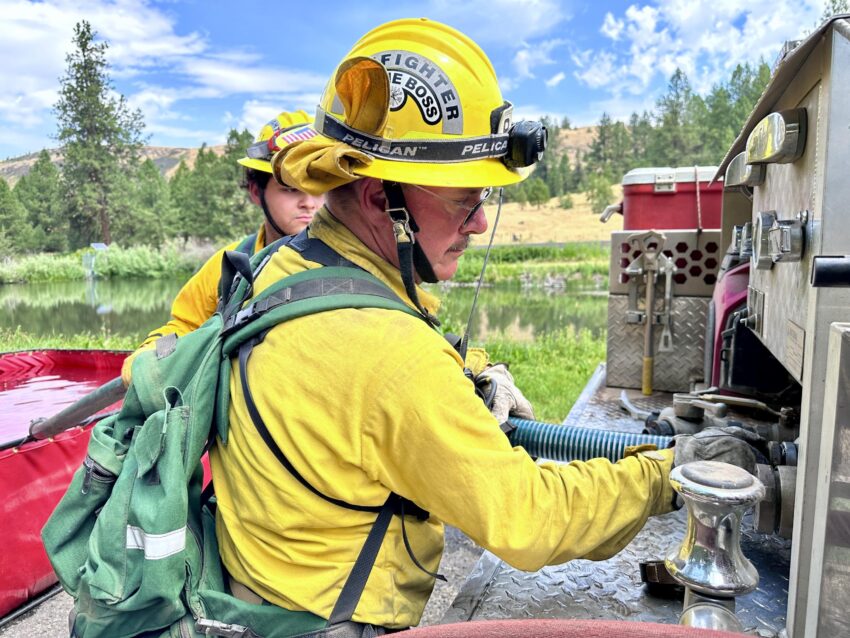 A firefighter hooking up a hose to a water pump.