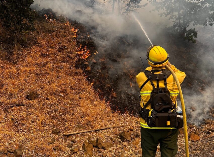 A firefighter shooting water from a hose on the Larch Creek Fire