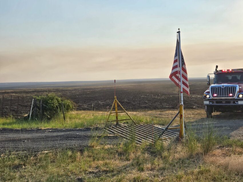 An American flag flying in the foreground with burnt earth in the background.