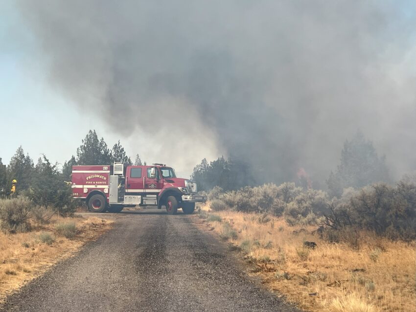 A fire engine parked on the road with smoke coming from the right side of the picture