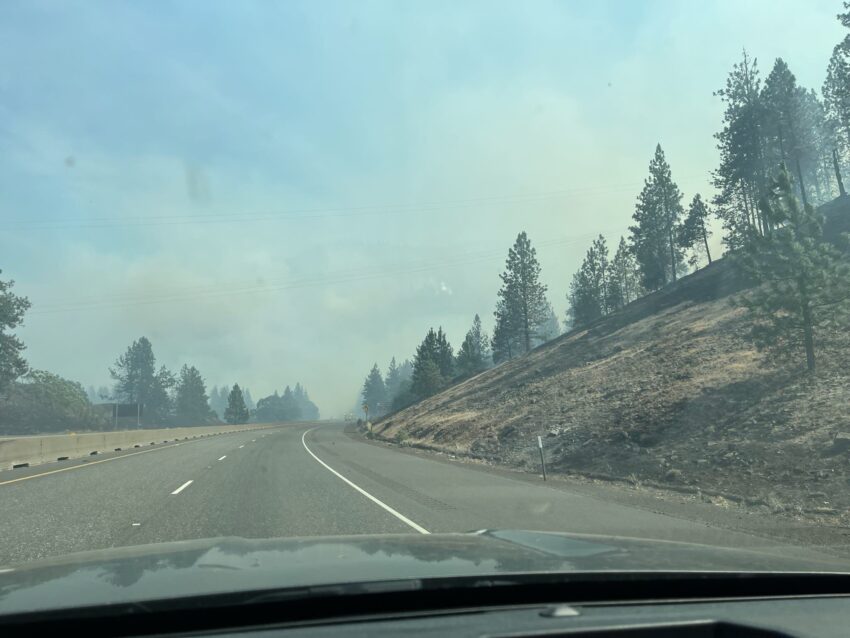 A photo of the landscape from inside a vehicle. There is significant smoke in the background.