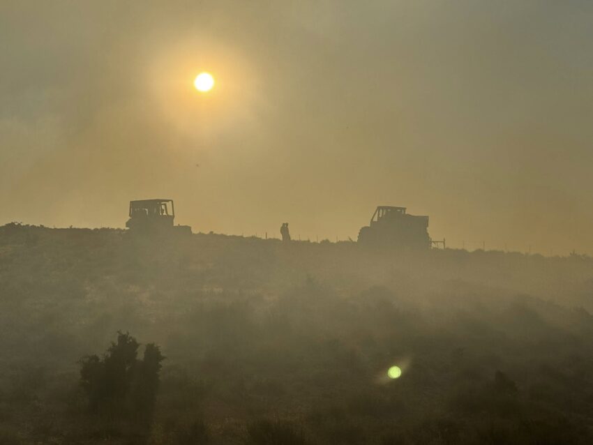 Fire equipment is in the distance with heavy smoke and the sun peeking through.