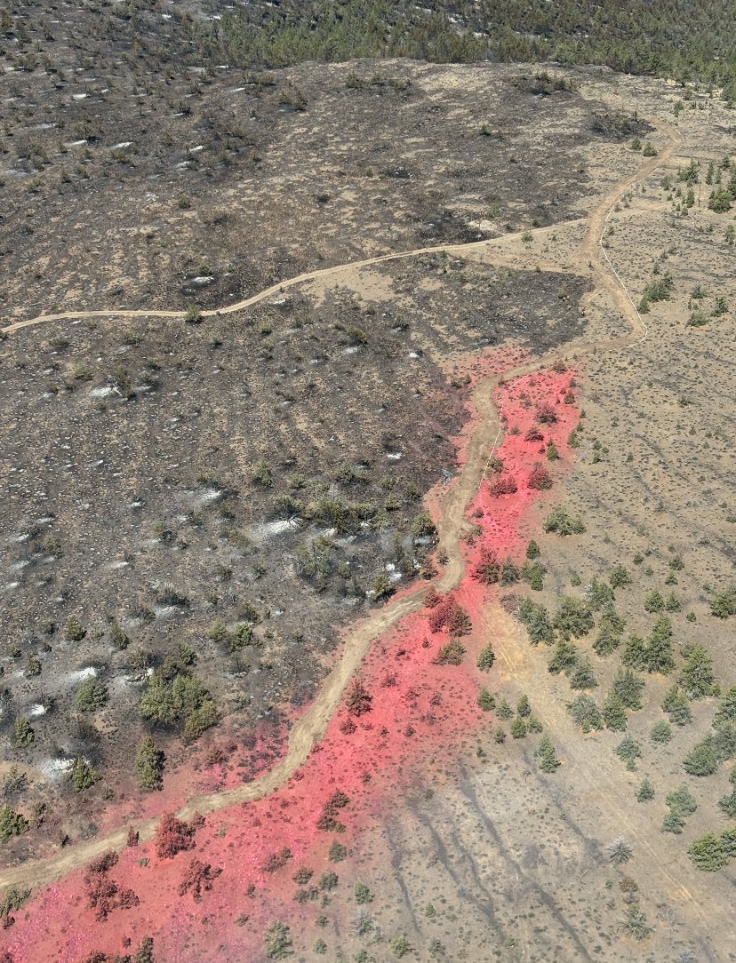 A photo of the landscape from the air showing bright red fire retardant from a plane on the Highland Fire.