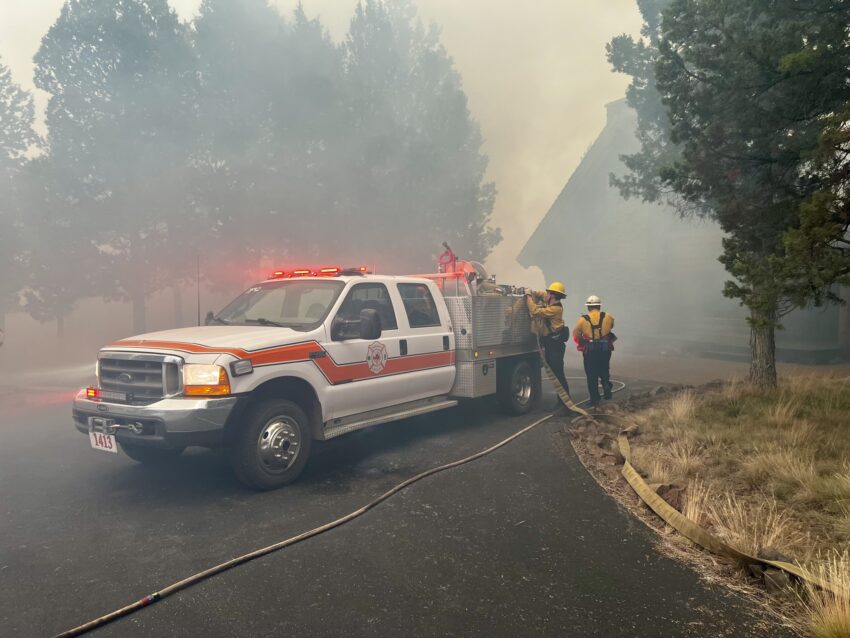 Two Firefighters are working at the Flat Fire with a water tender next to them.