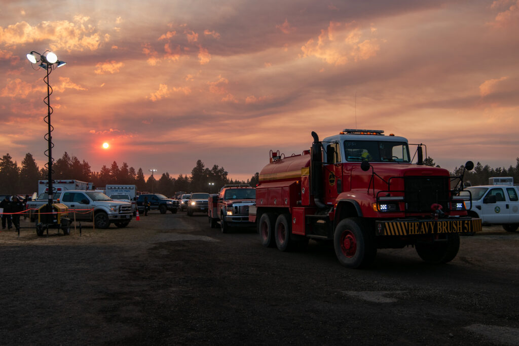 A water tender with the sun setting though smoke in the background.