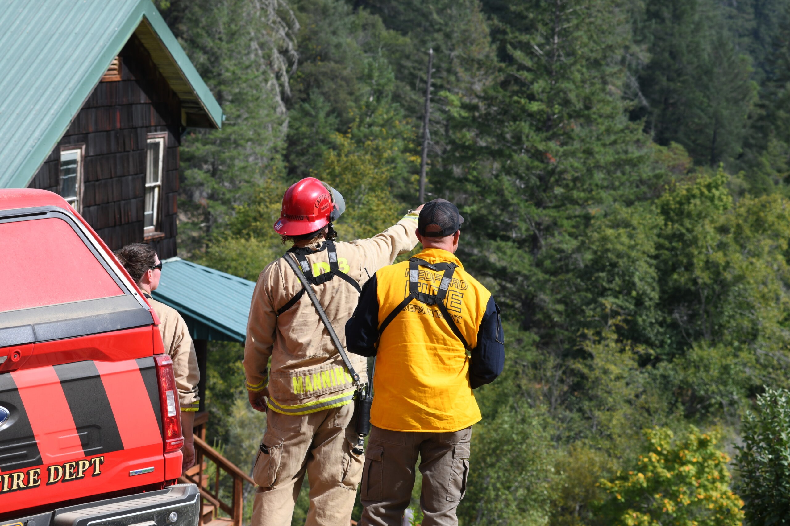 Three firefighters standing on a ridge pointing. A red truck is sitting in the foreground