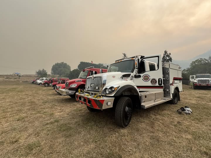 A fire engine parked on grass with smoke in the background.